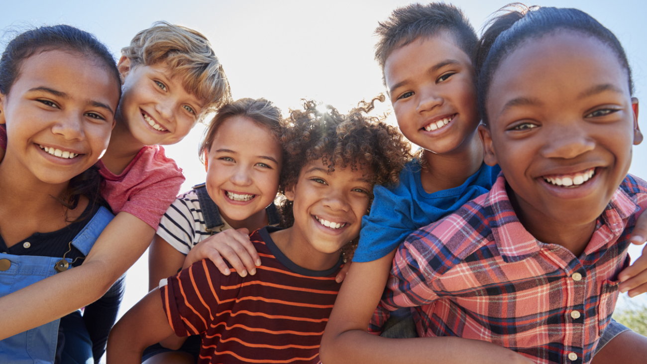 Six pre-teen friends piggybacking in a park, close up portrait